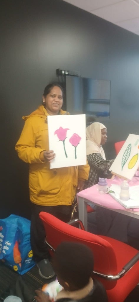 A woman holding a canvas of two pink roses painted at a Womenion session